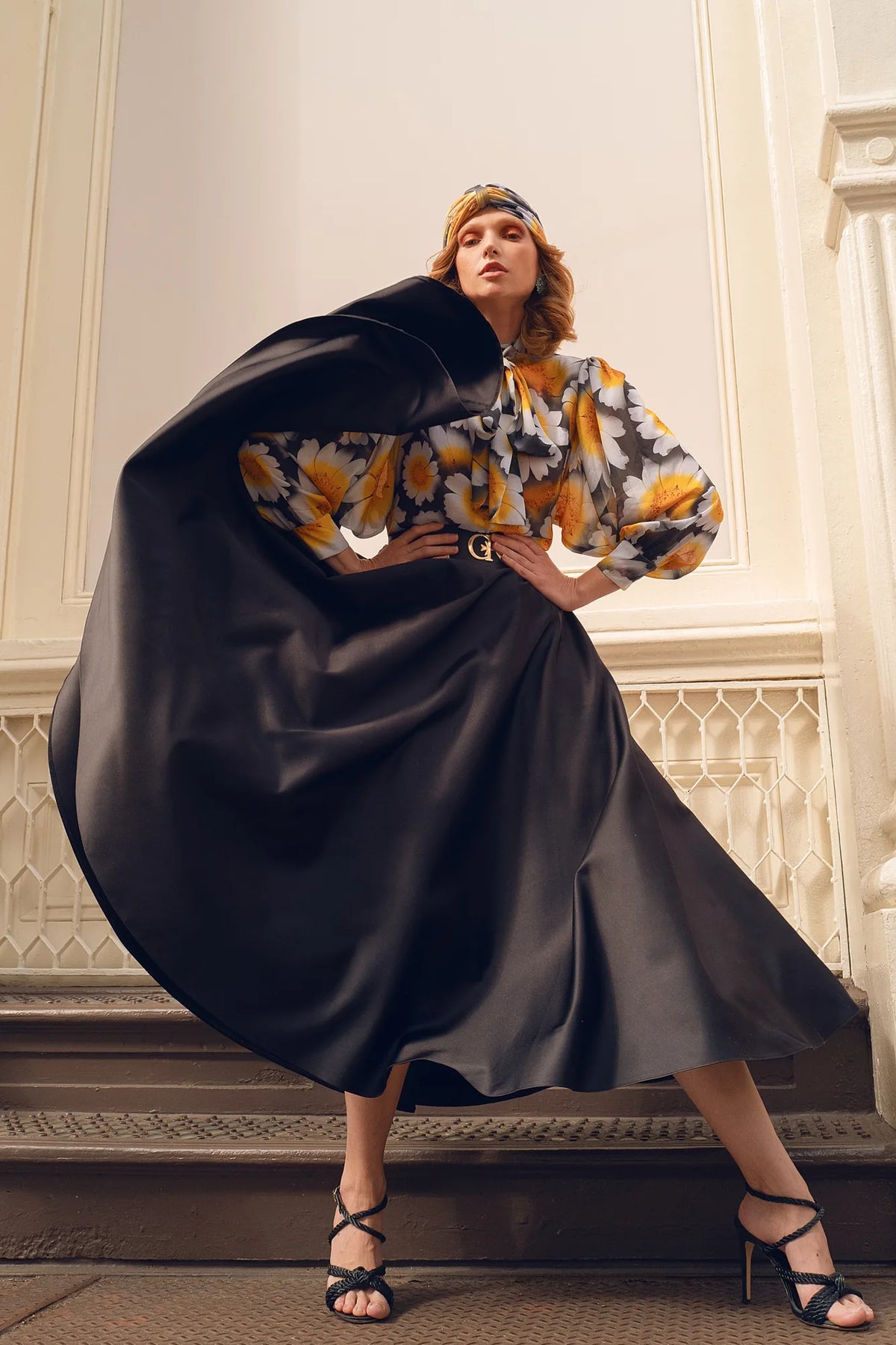 FRAQAIR black satin circle skirt swept out like a cape over a daisy print blouse and turban