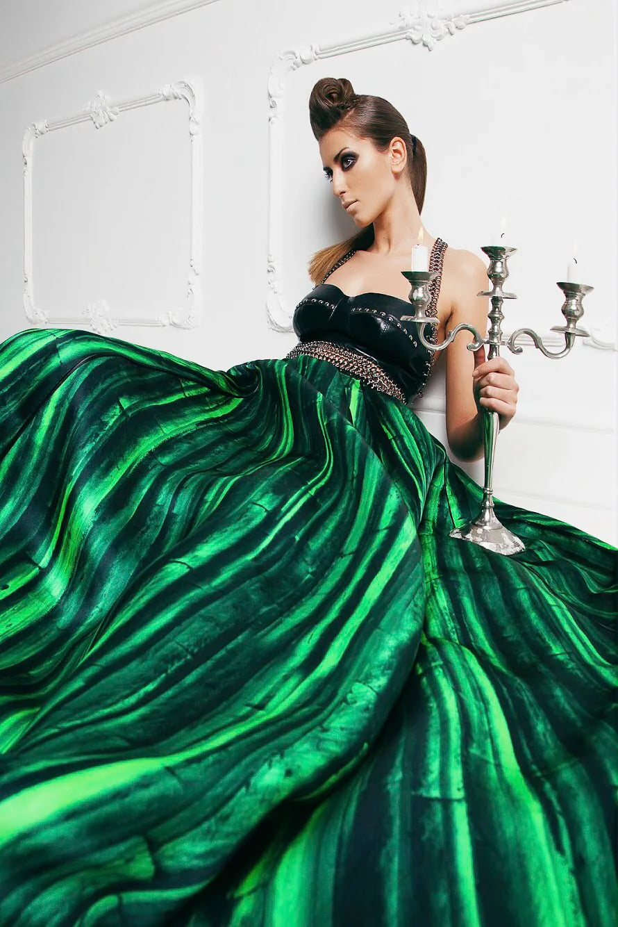 FRAQAIR by Nadia Fraqair: green stripe ball gown with a studded leather bustier, the model holding a silver candelabra against a white stucco wall