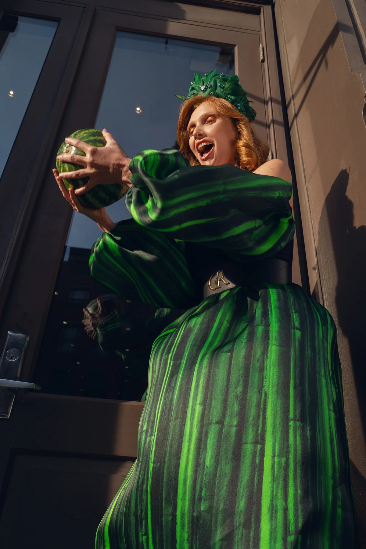 FRAQAIR green stripe gown, the model laughing as she lifts a watermelon in a doorway