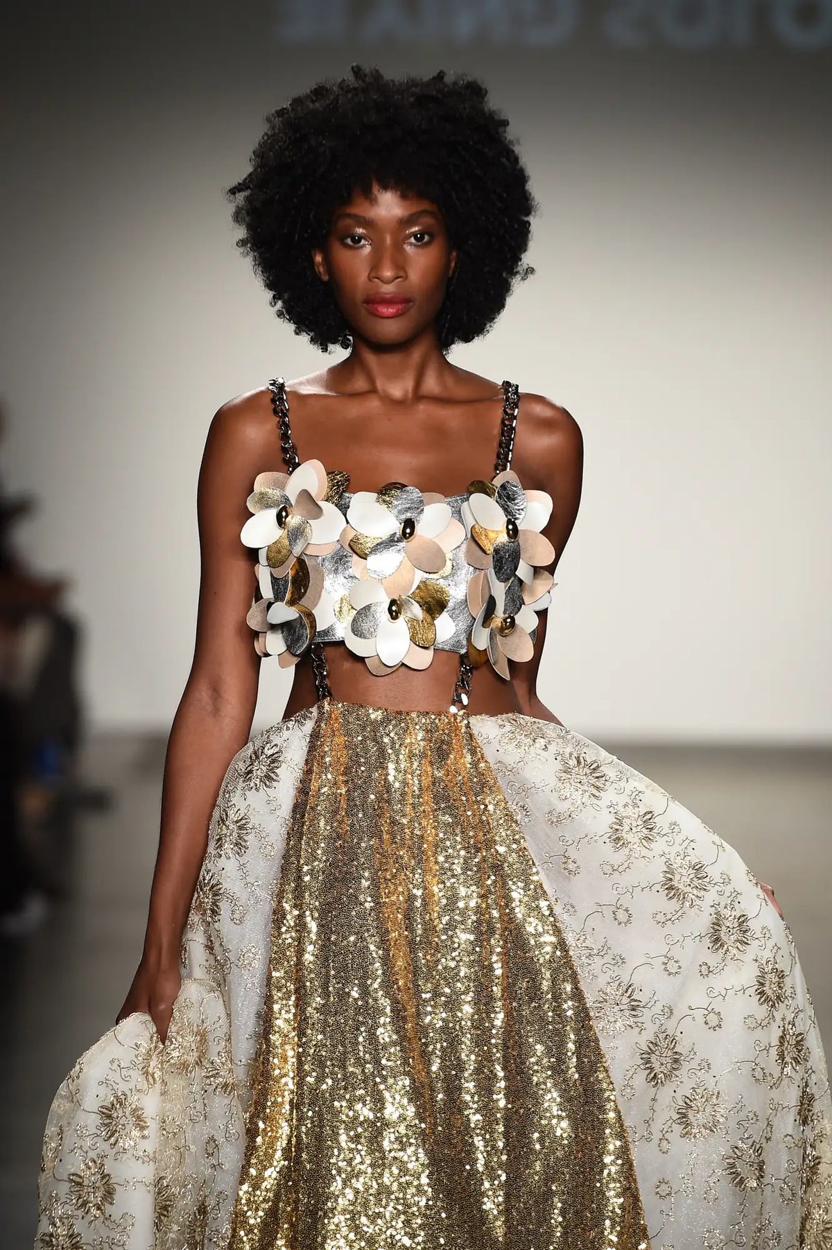 FRAQAIR on the runway, close up: a bustier of silver, gold and blush leather flowers on chain straps over a gold sequin skirt