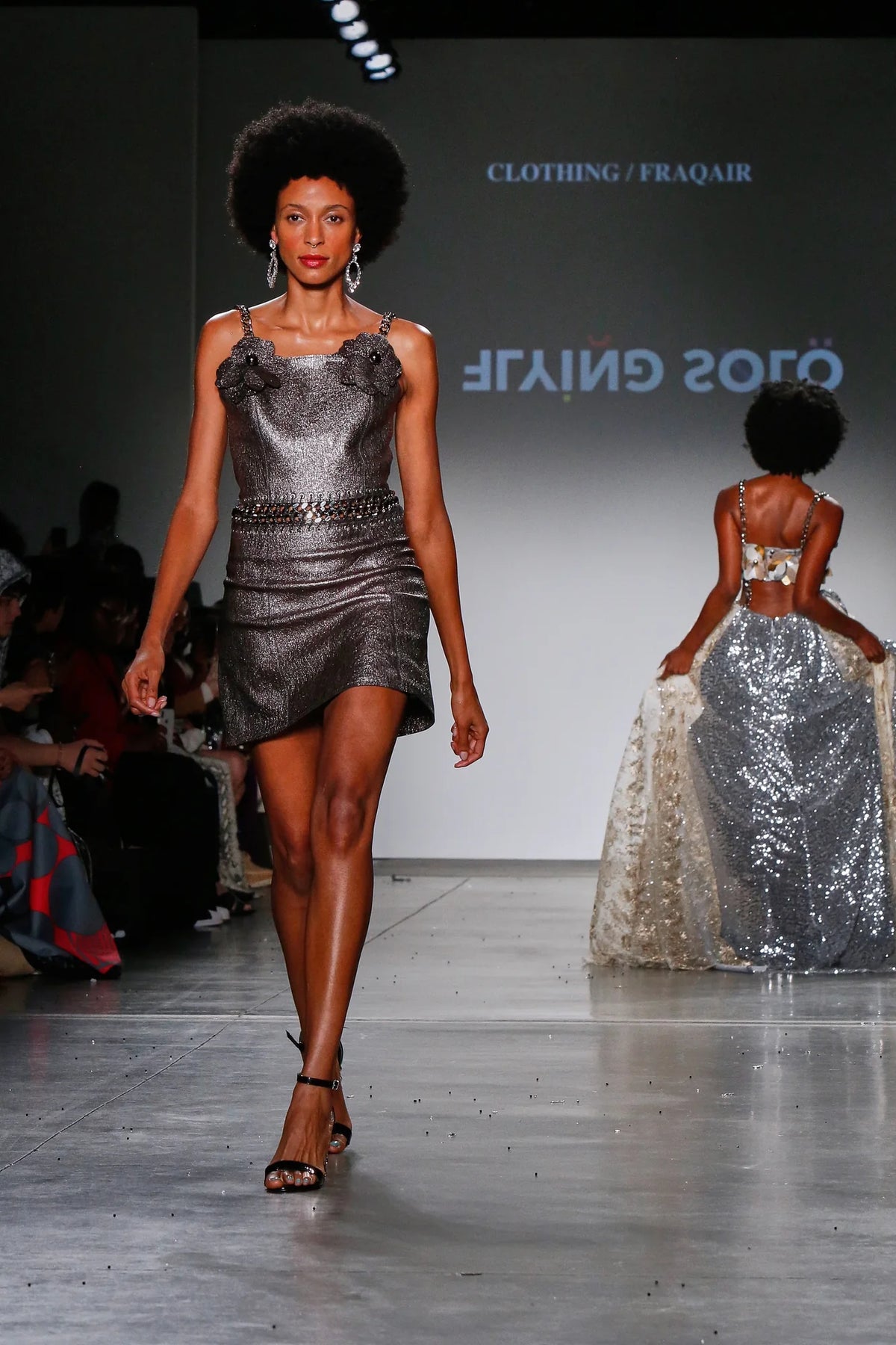 FRAQAIR on the runway at fashion week: metallic dress with leather flowers and chain straps, the house name on the screen behind