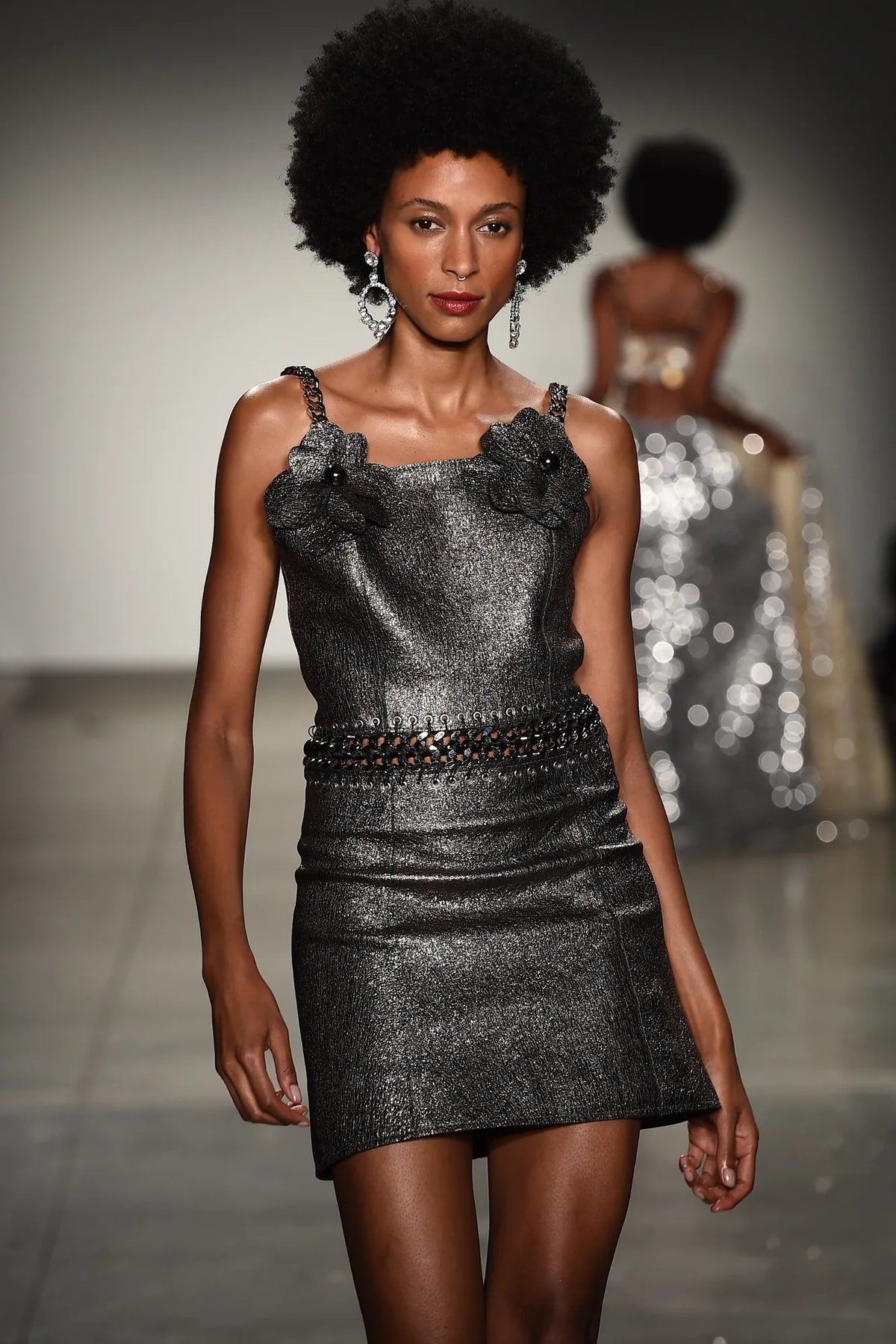 FRAQAIR on the runway, close up: a metallic dress with leather flowers at the neckline, a woven chain belt and crystal earrings